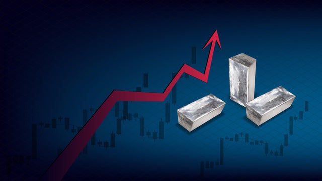 Metal price growth concept with isometric metal chunks and red up arrow on blue background. Candlestick charts up in background. 