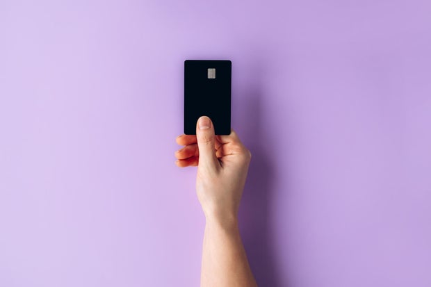 Female hand holding a black credit card against a pastel purple background for payment or finance concept