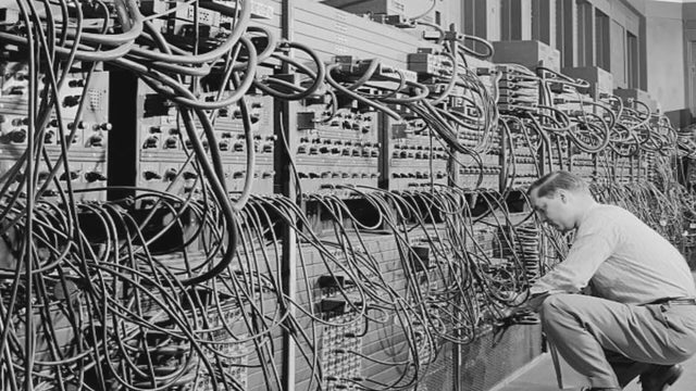 A man working on the ENIAC, a huge computer with many wires coming out 