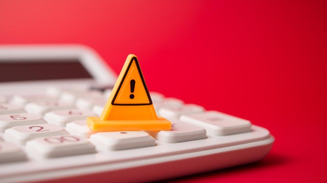 Yellow warning sign on white calculator with red background copy space. 