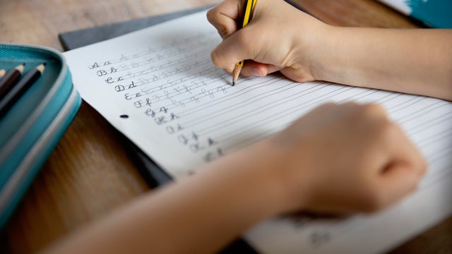 Over the shoulder view of child (8-9) using a pencil to practice handwriting the letters of the alphabet in cursive script 