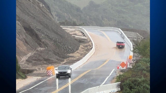 Two vehicles on a highway that has rock debris obstructing the lanes 