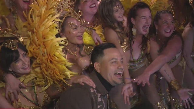 Several women in Carnaval outfits pose for a photo with a man 
