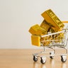 Gold bars in shopping trolley on wooden table with white wall background copy space. 