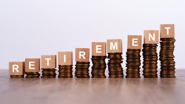 Retirement Word on Wooden Block with Stacked Coins on White Background 