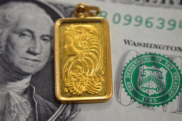 A closeup view of American dollars USD money banknote and Lady Fortuna motif on a gold bar pendant, 24K Gold Bar, pure fine gold 999.9, for investment or savings 