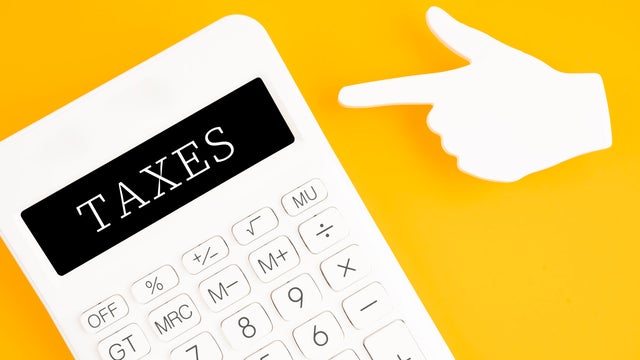 Taxes written on a calculator with sticky note finger shape on yellow background. 