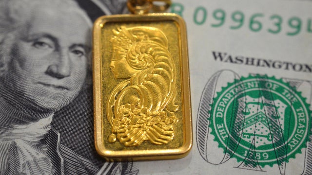 A closeup view of American dollars USD money banknote and Lady Fortuna motif on a gold bar pendant, 24K Gold Bar, pure fine gold 999.9, for investment or savings 
