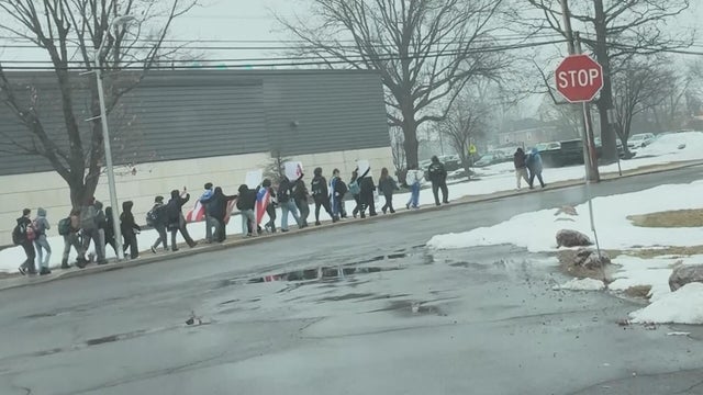 Students walk along a sidewalk holding flags and signs in Quakertown in February 