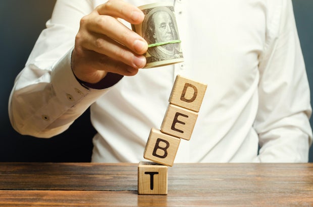 Businessman removes wooden blocks with the word Debt. Debt relief or cancellation is the partial or total forgiveness of debts, or the slowing or stopping growth. Restructuring. Pay. Selective focus 