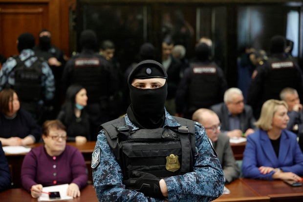 A court bailiff stands guard as defendants accused in the deadly 2024 Crocus City Hall music venue gun attack stand in glass boxes during the announcement of their verdicts in Moscow, March 12, 2026. 