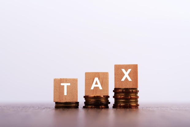 Tax Word on Wooden Block with Stacked Coins on White Background 