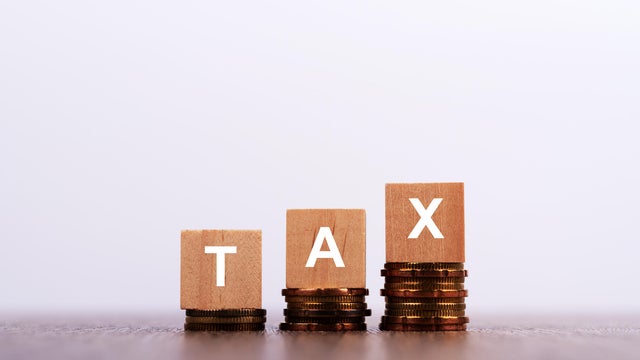 Tax Word on Wooden Block with Stacked Coins on White Background 