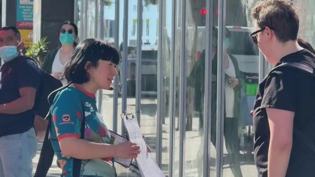 A woman holds a clipboard in front a person while trying to collect signatures 