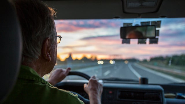 Senior man driving a car on a highway at sunset 