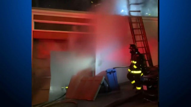 A firefighter walks in front of a structure that has smoke coming out of it 