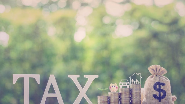 Understanding the Impact of Taxes on Savings and Investments: The word TAX displayed alongside stacks of coins with several icons on top e.g. a piggy bank, a sprouting plant, a car and a family house. 