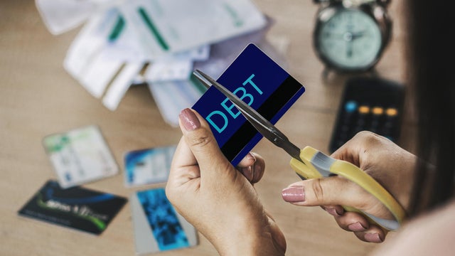 woman hand cutting credit cards by scissors with calculator and financial bills on desk 