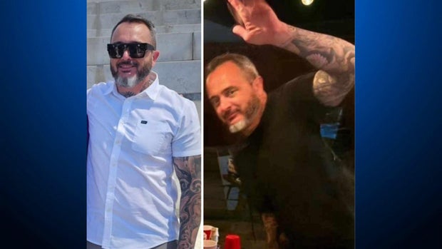 A man wearing a black short sleeve shirt raising his left hand which is covered with tattoos 