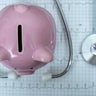Piggy bank with stethoscope on illustration of wave form on checked ecg graph background, health saving account, insurance, top view 