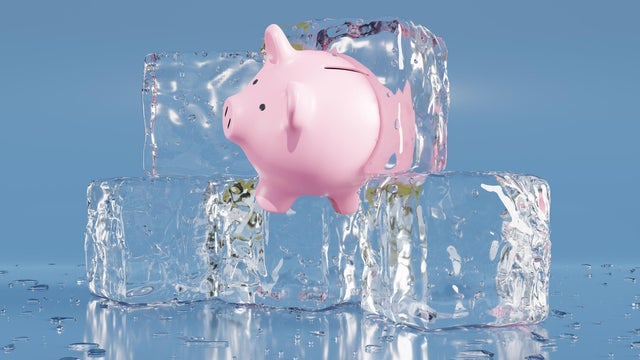 Pink piggy bank partially in an ice cube on blue background. Illustration of the concept of confiscated and impounded illegal assets, frozen assets and economic stagnation 