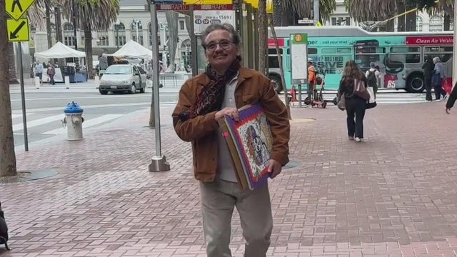 A man carrying artwork in between his arm walking on a city sidewalk 