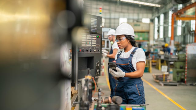 Female apprentice engineer working with CNC machine in factory 