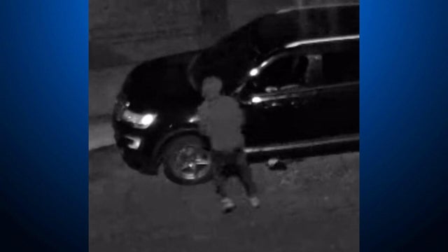 A man walking backwards away from a vehicle with a shattered driver's side window 