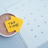 Tax time concept. Reminder sticker on clock and calendar background 