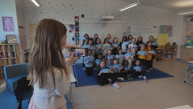 A student takes a photo of a class holding up their boarding passes, showing their names were taken to space 