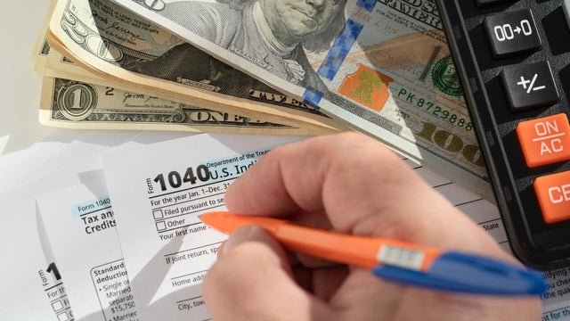 Person filling out US 1040 tax form with cash and calculator 
