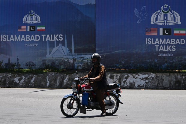 A commuter rides past a billboard for the U.S.-Iran peace talks in Islamabad on April 13, 2026.