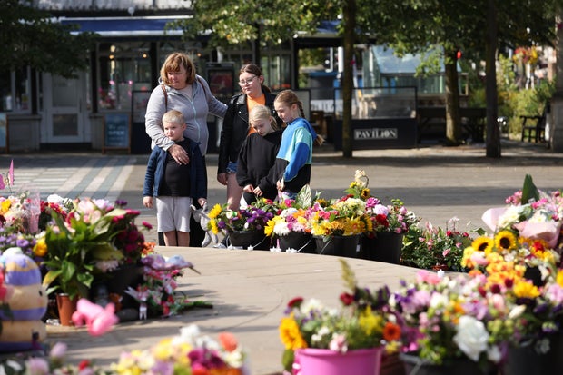 A family looks at flowers and tributes for the three girls who died in a knife attack at a dance class in Southport, England, Aug. 23, 2024. 