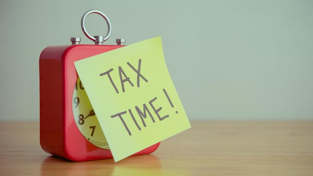 Red alarm clock with TAX TIME paper note on wooden table white wall background copy space. 
