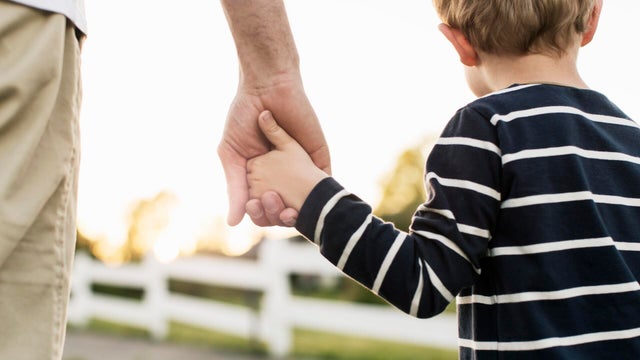 Rear view of father and son holding hands while standing outdoors 