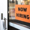 "now hiring" sign posted on business door 