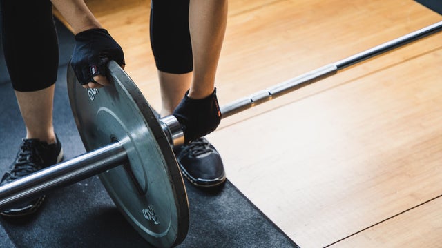 asian woman lifting weights in a gym- changing barbell weight plate 