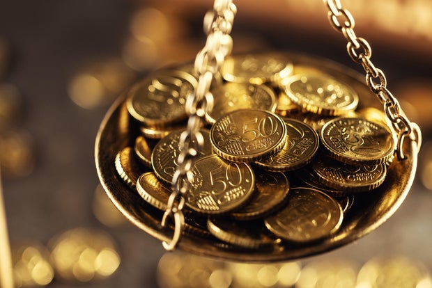 Antique brass scales, one pan filled with gold coins, tilted towards wealth. In the blurred background, a wooden gavel and other coins are present, evoking the theme of justice, law and money. Close-up 