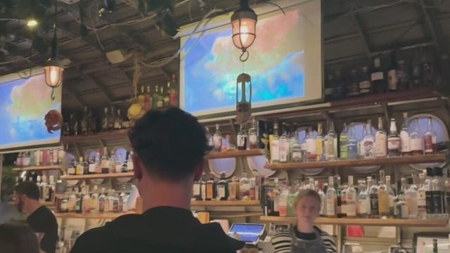 a projector screen showing a TV show above a bar 
