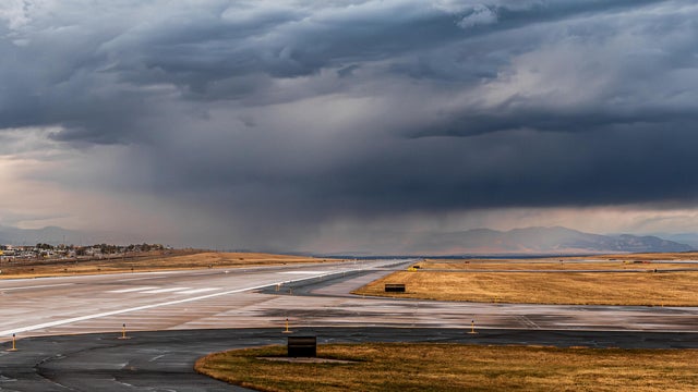 Clouds loom over a vast airport runway, indicating an approaching thunderstorm 