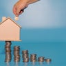 Hand inserting coin into house model on top of coins stacks. Save and investment money concept. 