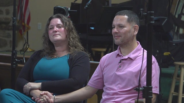 Angela and Carlos Della Valle speak to a reporter in a church 