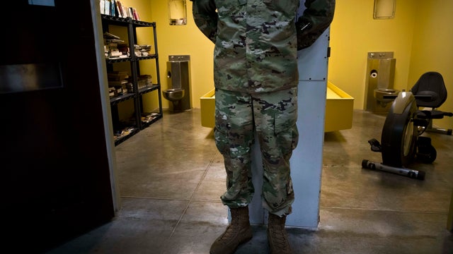 In this photo reviewed by U.S. military officials, a U.S. soldier stands between two cells, one used as a library and the other a gym, inside the Camp VI detention facility at the Guantanamo Bay U.S. naval base in Cuba on June 6, 2018. 