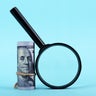 Magnifying Glass and Money Roll on Blue Background 
