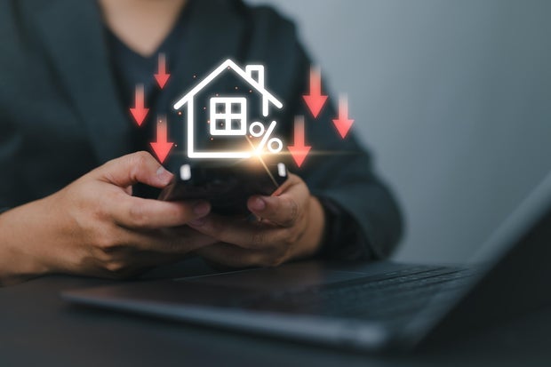 Businessman use smartphone with virtual home icon and down arrow for economical real estate and lower mortgage interest rates. Reduced prices for rental housing, Demand for home purchases decreases.