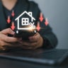 Businessman use smartphone with virtual home icon and down arrow for economical real estate and lower mortgage interest rates. Reduced prices for rental housing, Demand for home purchases decreases. 