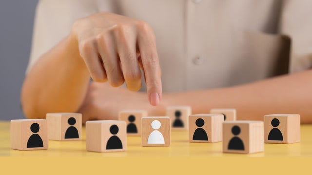 Selection of people to work in the company ,Managers choose people to do the right job for the job ,People symbol on wooden block ,Finger points to the correct option ,Different from others. 