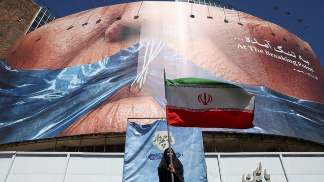 A woman holds an Iranian flag near an anti-U.S. billboard depicting U.S. President Donald Trump and the Strait of Hormuz, in Tehran 