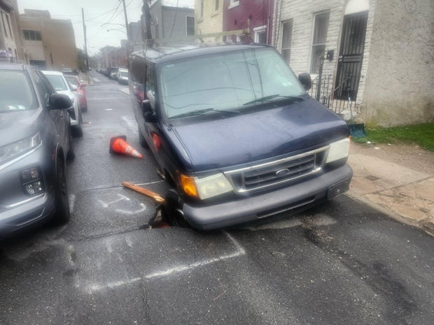 The front passenger tire of a van is lodged in a sinkhole on a North Philadelphia street
