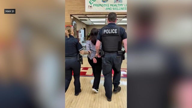 Woman being escorted out of school gym in handcuffs 
